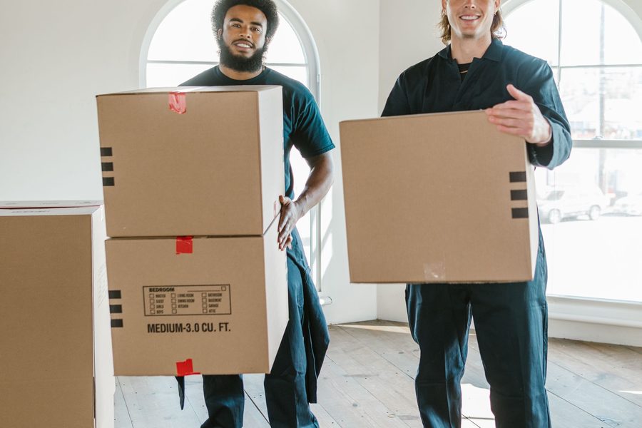 Two movers carrying boxes through a bright, empty living room