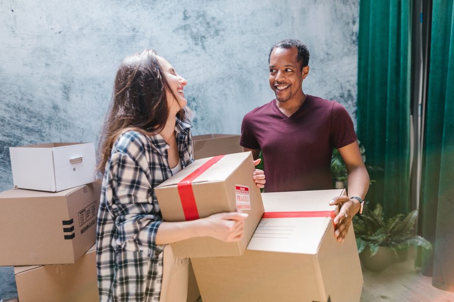 A couple carrying taped moving boxes in their new home