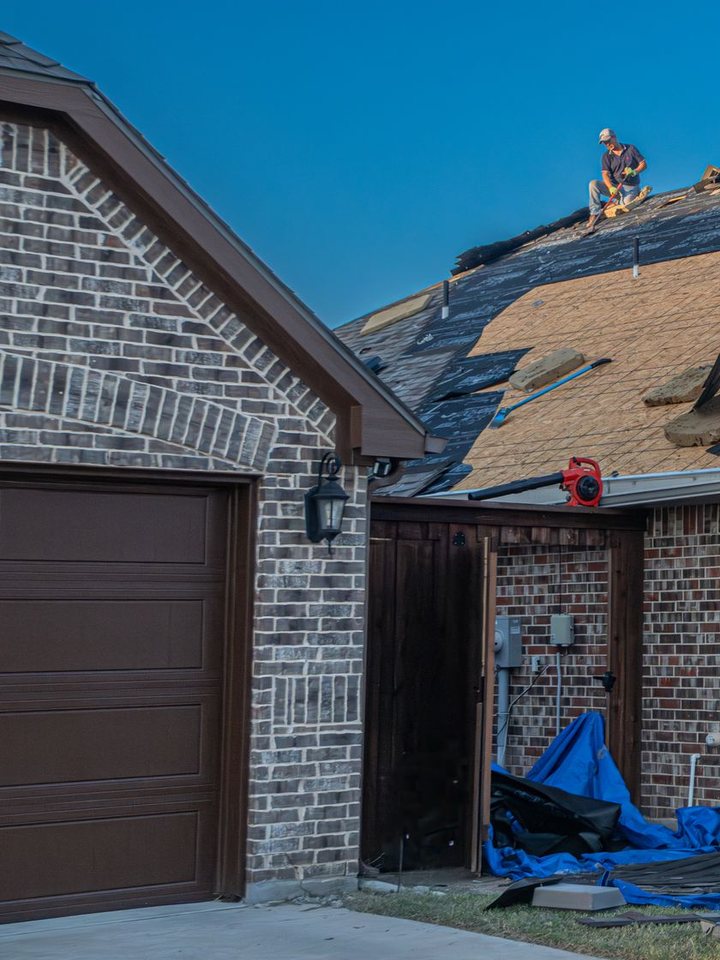 A brick house with a garage, mid re-roof, a roofer at the ridge