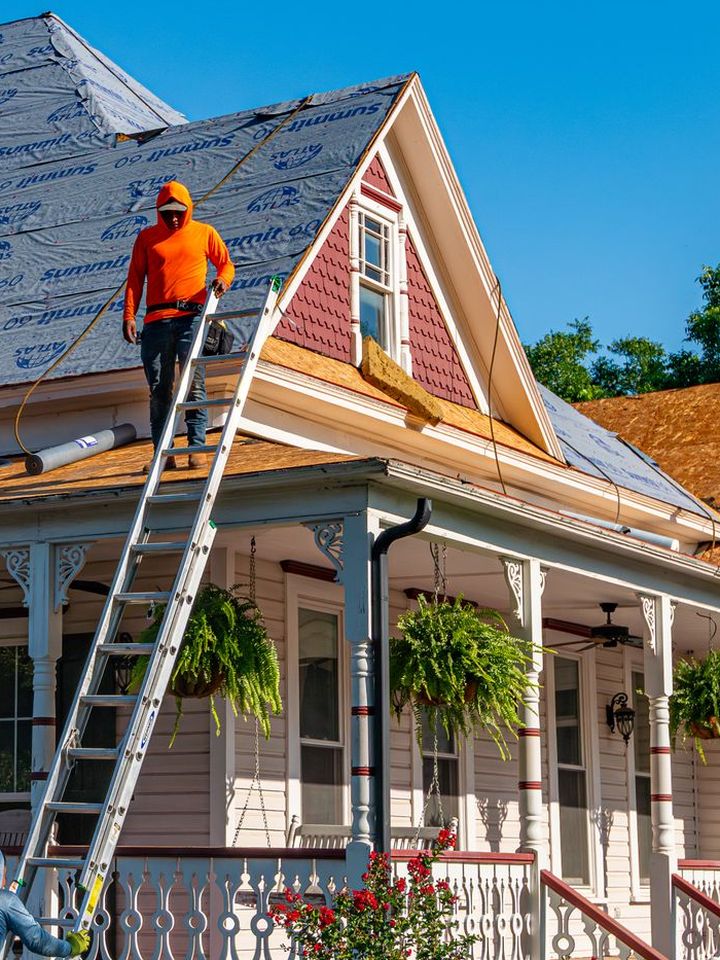 A roofer on a ladder at the gutter of a porch house with new underlayment