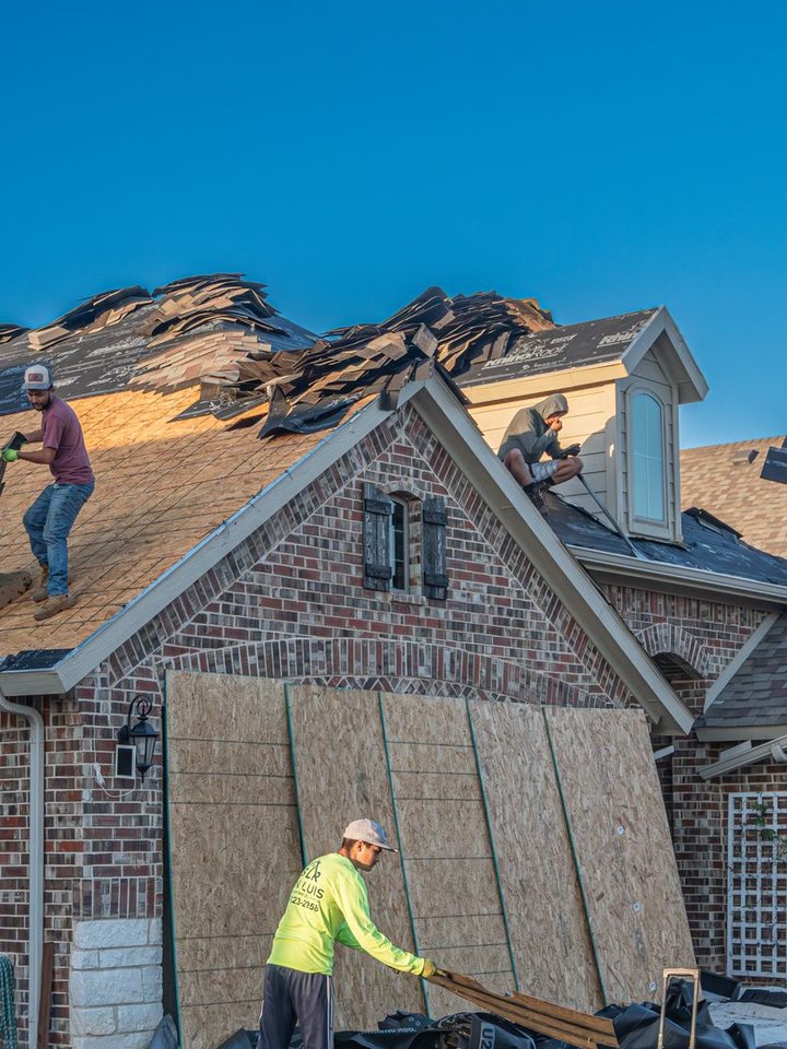 Roofers tearing off old shingles above a brick gable