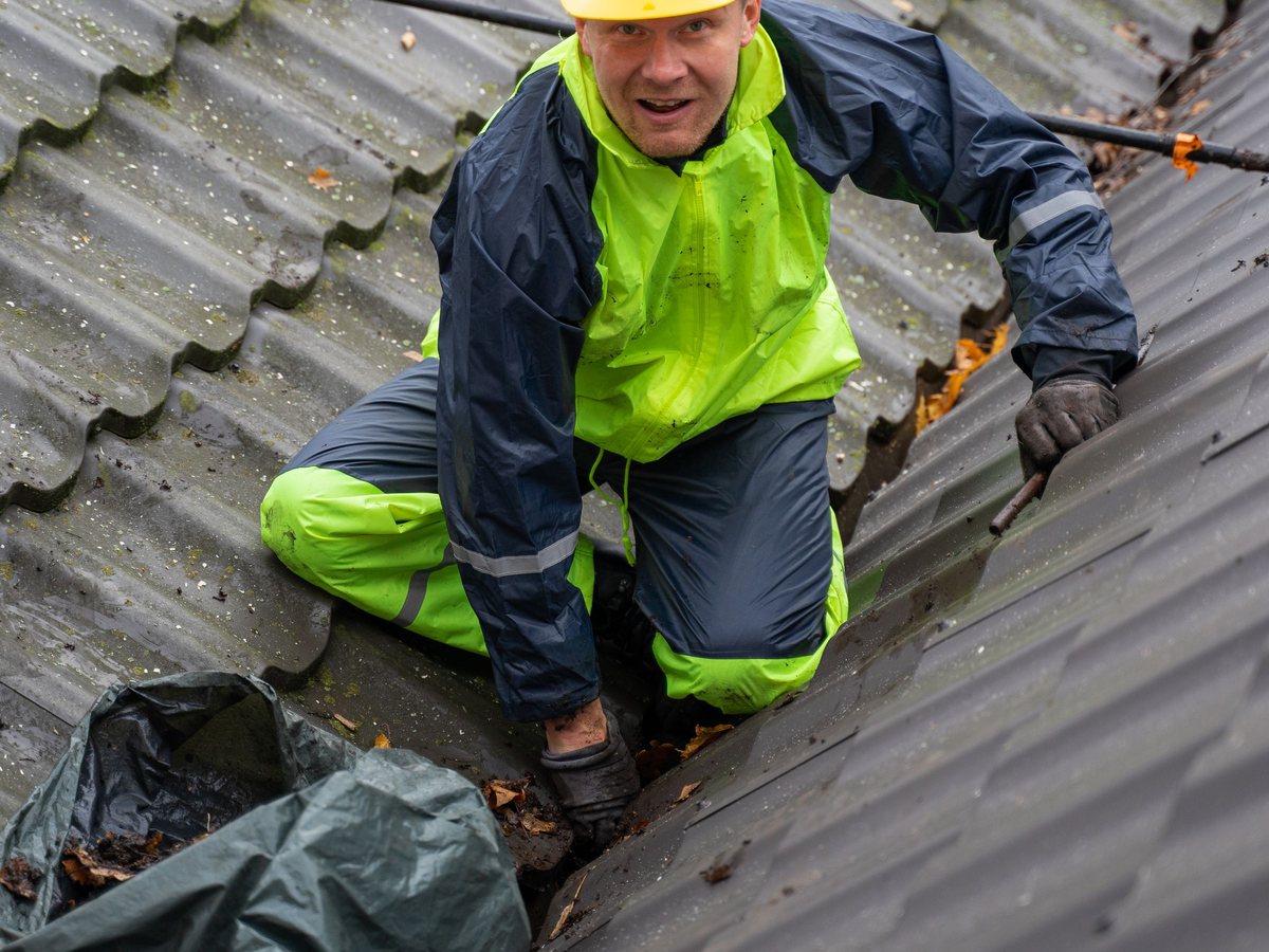 A roofer in a hard hat and high-visibility jacket kneeling on a roof beside a tarp
